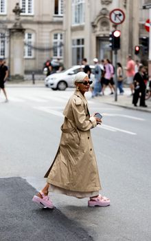 Stylish woman wearing trench coat crossing a busy city street in Copenhagen, Denmark.