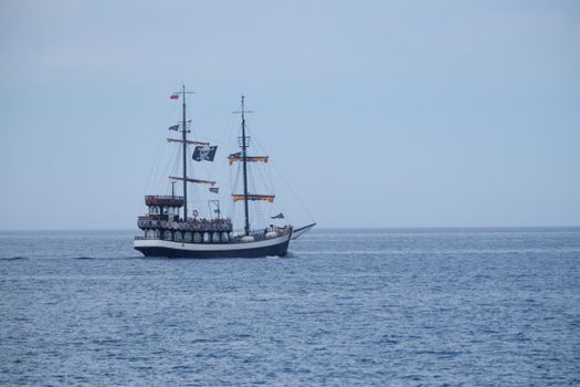 A vintage pirate ship with sails unfolds on calm ocean waters under a clear sky.