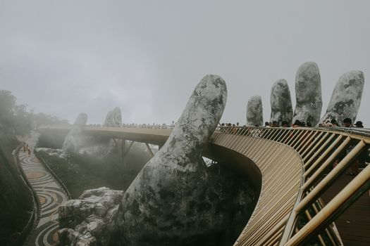 Stunning view of Golden Bridge held by stone hands enveloped in mist, Ba Na Hills.