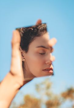 一个宁静的女人在明亮的蓝天下，用一面镜子反射着阳光