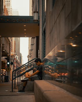 A man sits on city steps, engaged with his smartphone, reflecting the urban environment around him.