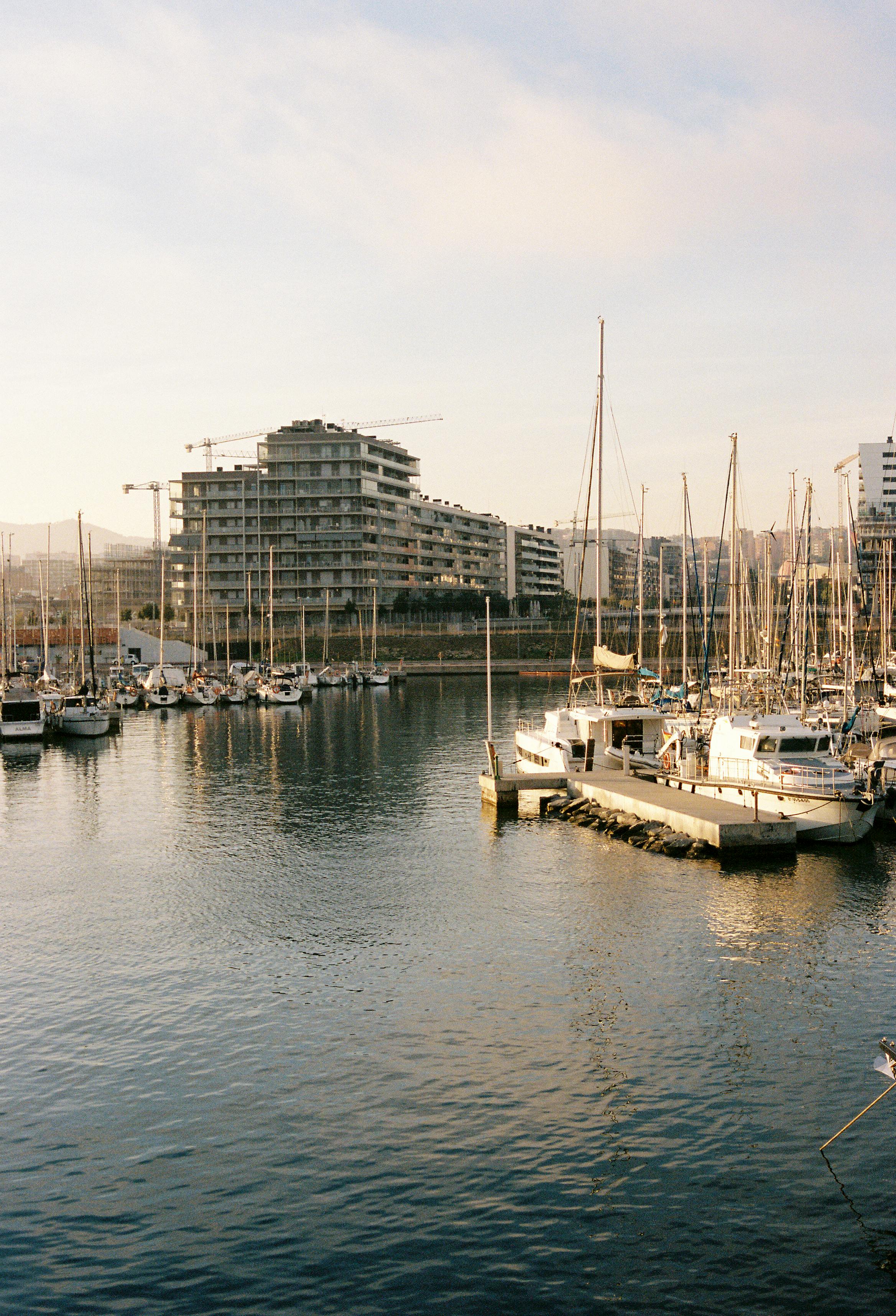 Beautiful harbor view with moored sailboats and modern buildings reflecting on calm waters at sunrise.
