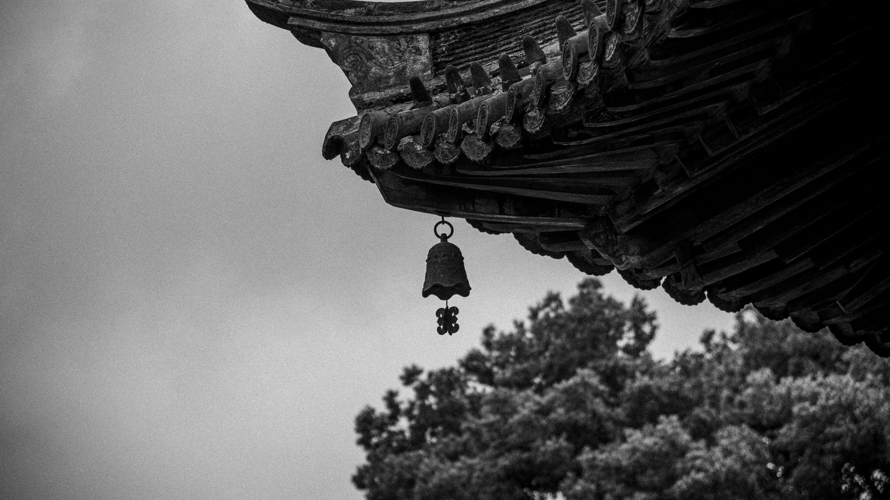 Close-up of a traditional temple roof with a hanging bell against a cloudy sky.