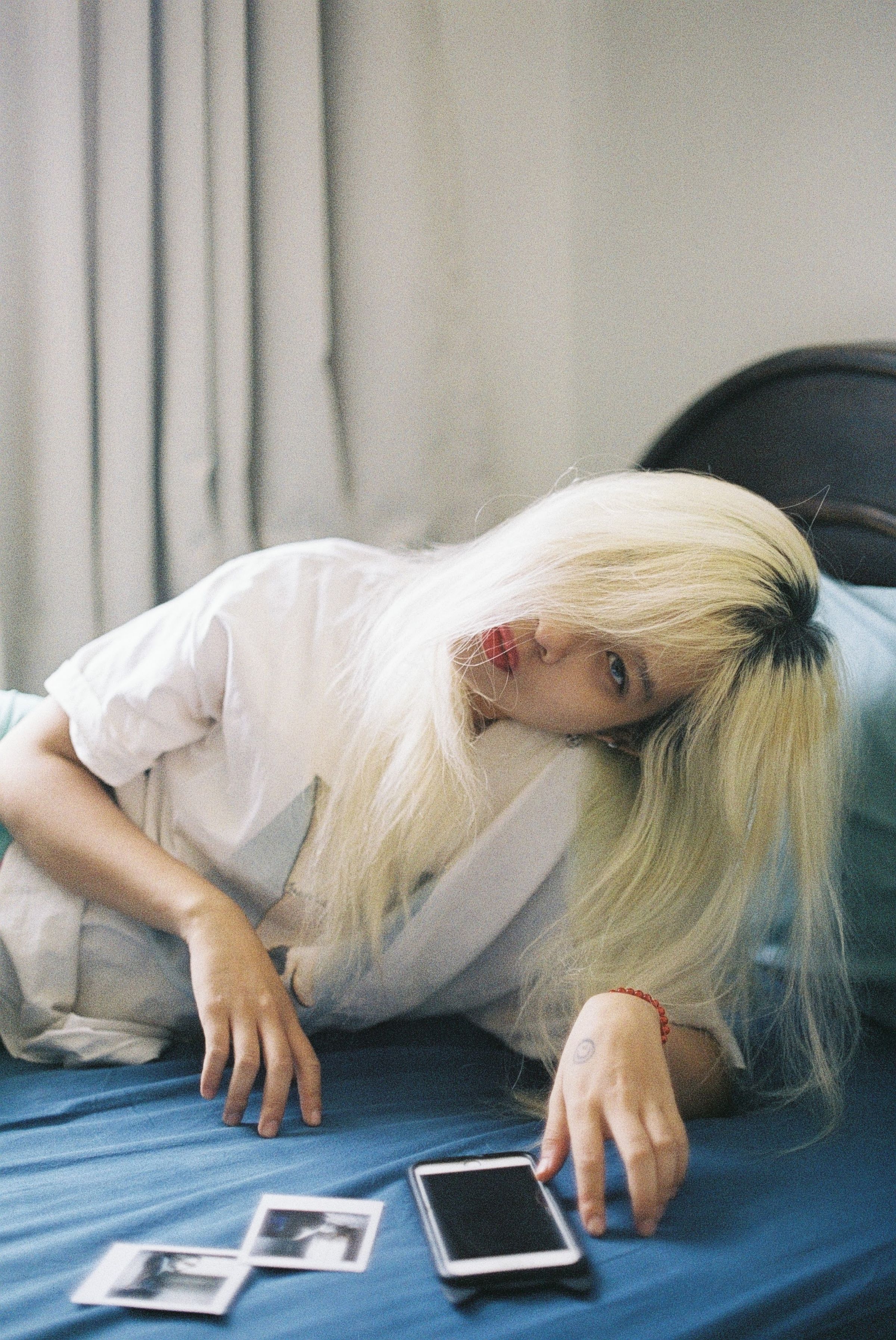 Blonde woman on bed with smartphone, embracing relaxation and leisure indoors.