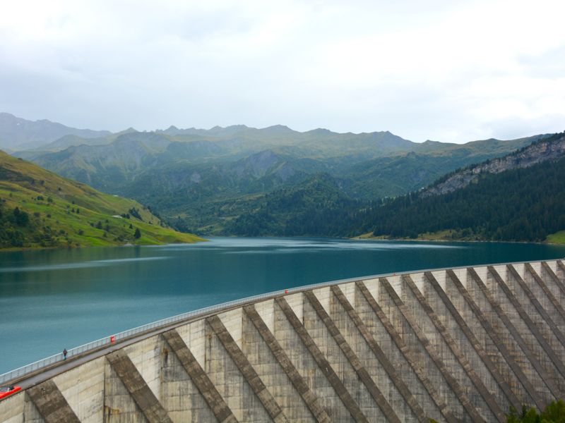 A large dam and calm lake reflecting forested mountains