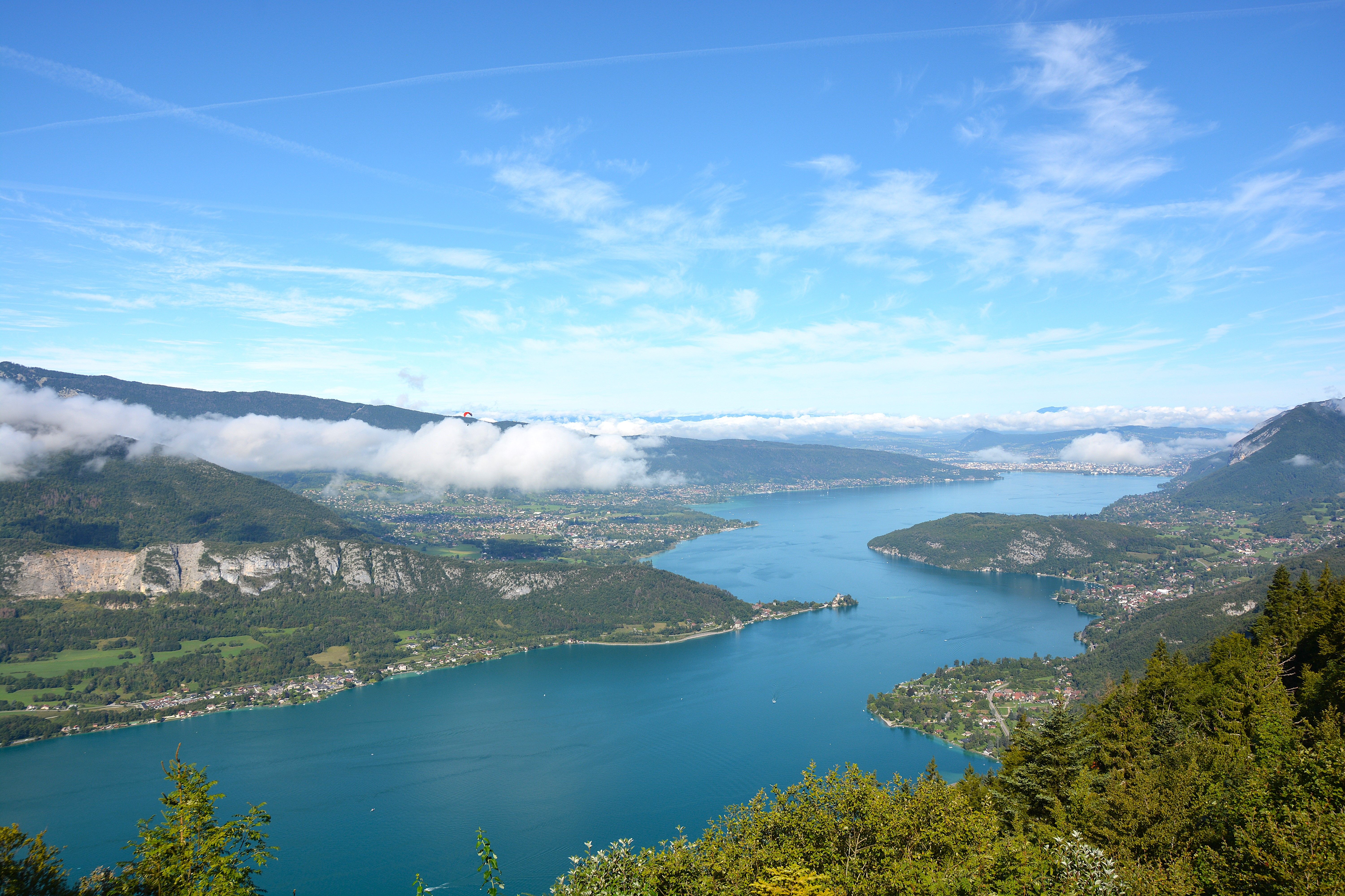 A breathtaking aerial view of Lake Annecy surrounded by lush forests and mountains under a clear blue sky.