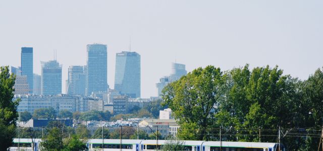 Skyline of Warsaw with modern buildings and a train passing amidst the greenery.