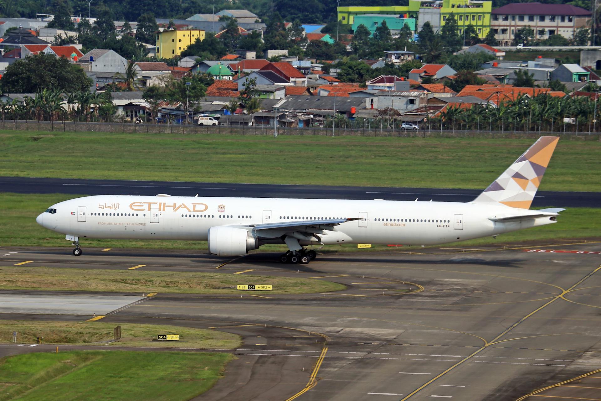 Etihad Airways aircraft taxiing on runway with cityscape backdrop.