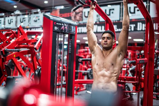 A muscular man exercising on gym equipment demonstrating strength and fitness indoors.