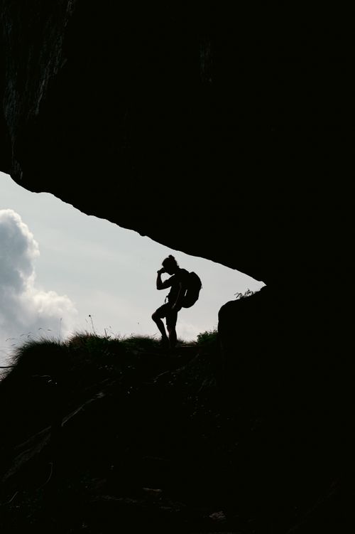 Free A determined climber silhouetted against the sky as they scale a rocky landscape at sunset. Stock Photo