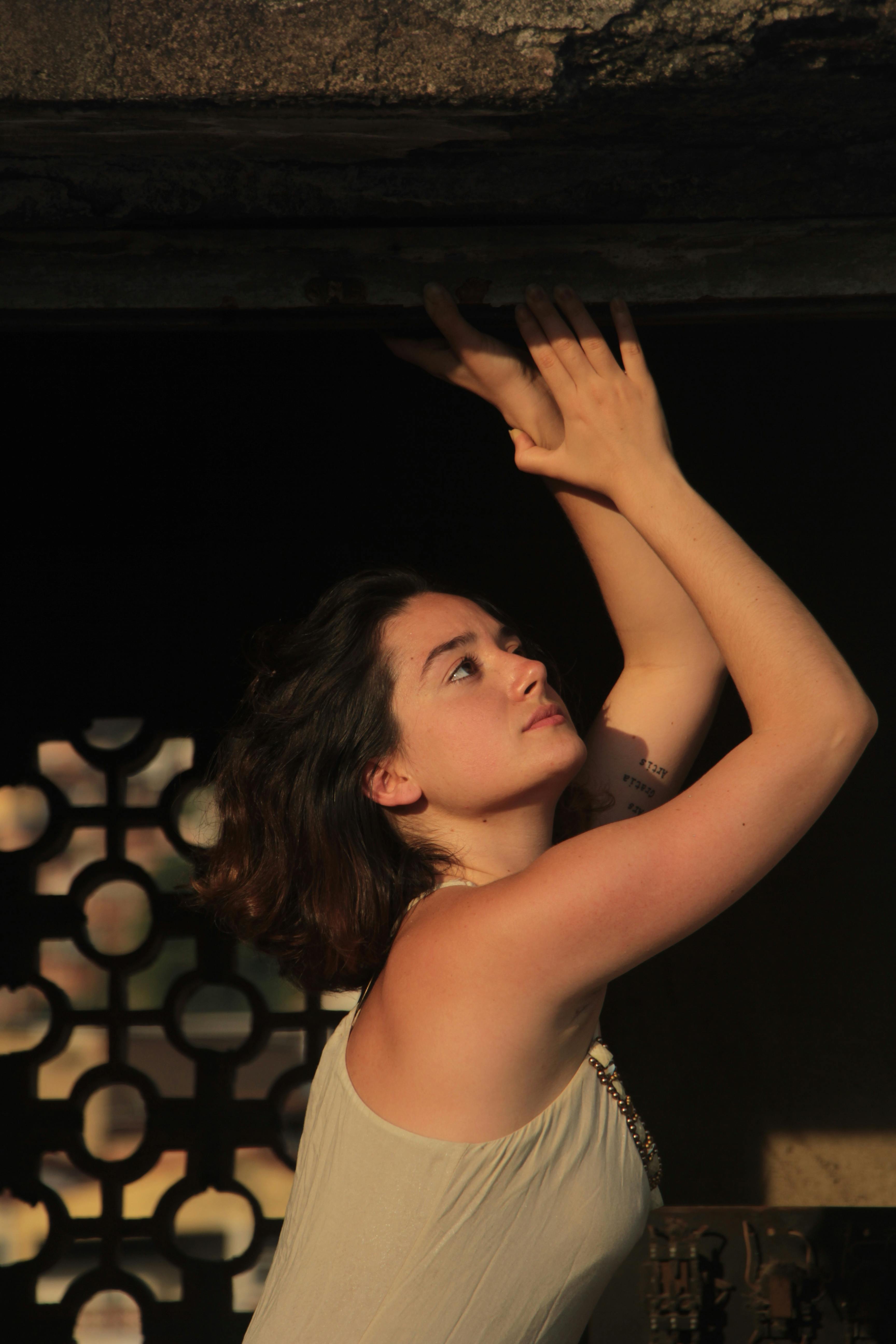 woman wearing white tank top holding on concrete ceiling