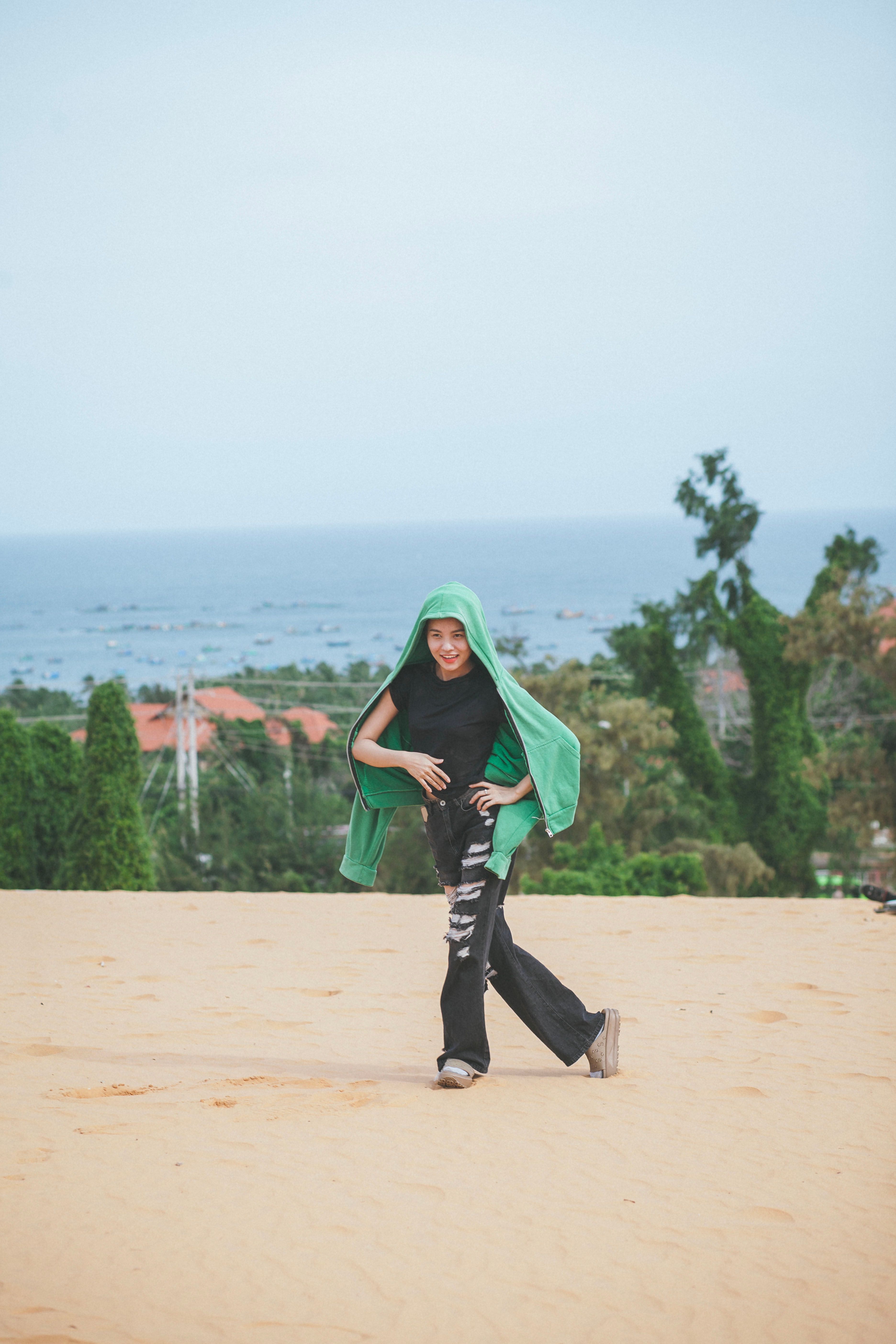 Teen wearing a hoodie running on a sandy beach with ocean and trees in the background, exuding joy and freedom.