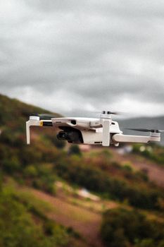A white drone captured in flight over a picturesque mountainous landscape with cloudy skies.