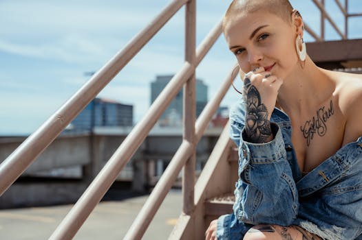 一位剃着光头、身穿牛仔夹克的纹身女子，在户外楼梯上自信地摆着姿势