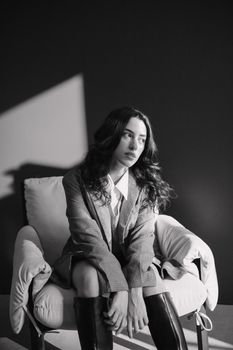 Stylish black and white portrait of a woman sitting on a chair in a studio setting.