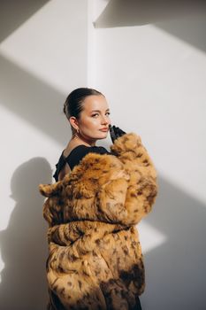 Stylish woman wearing a luxurious fur coat posing in a modern studio setting.