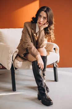 Portrait of a woman in stylish attire sitting in a studio with terracotta backdrop.