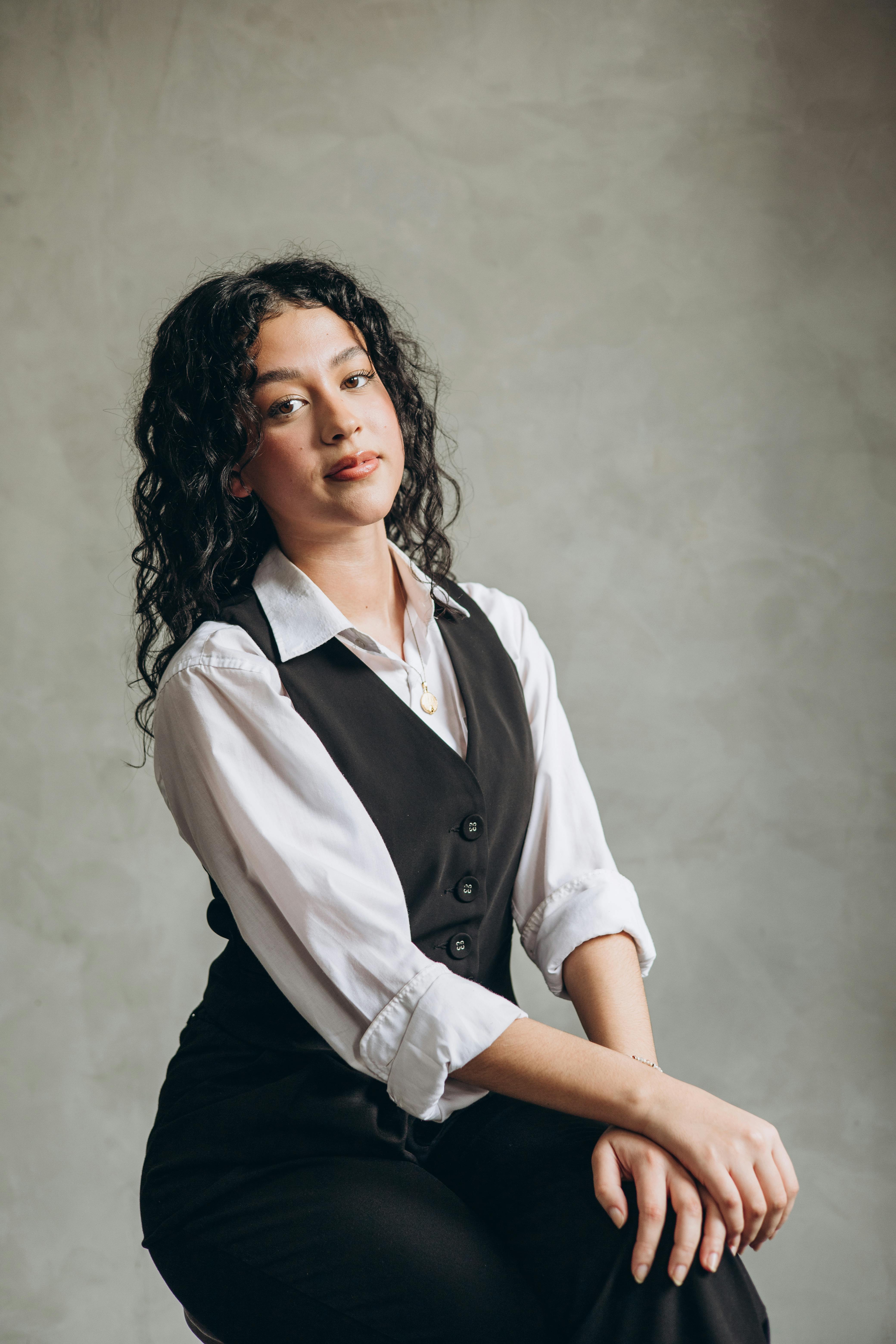 a woman in a black vest and white shirt sitting on a stool