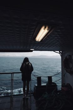 A woman stands silhouetted on a ferry overlooking the sea, during a moody day.