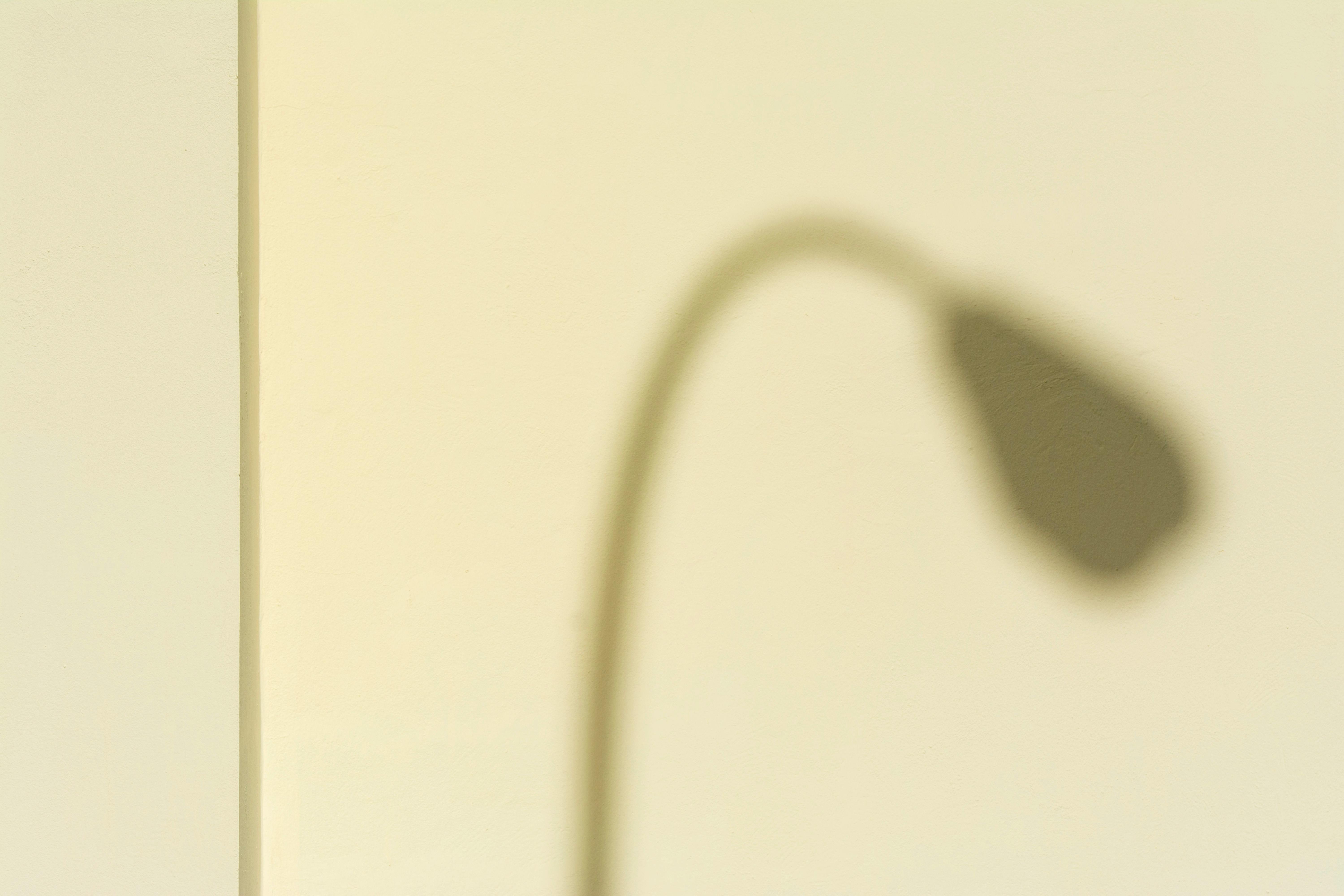 Free A minimalist photo capturing a lamp's shadow on a yellow wall, evoking simplicity. Stock Photo