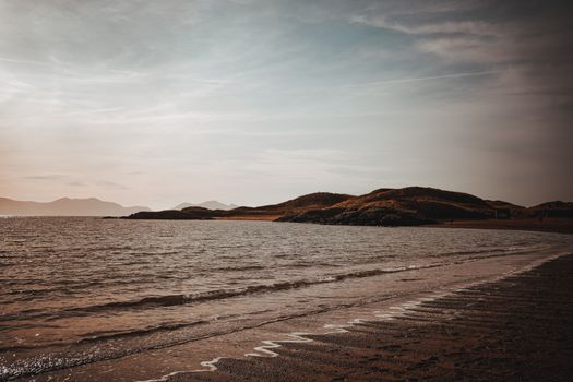 Serene view of Llanddwyn Island beach at sunset with golden hues and tranquil waters.
