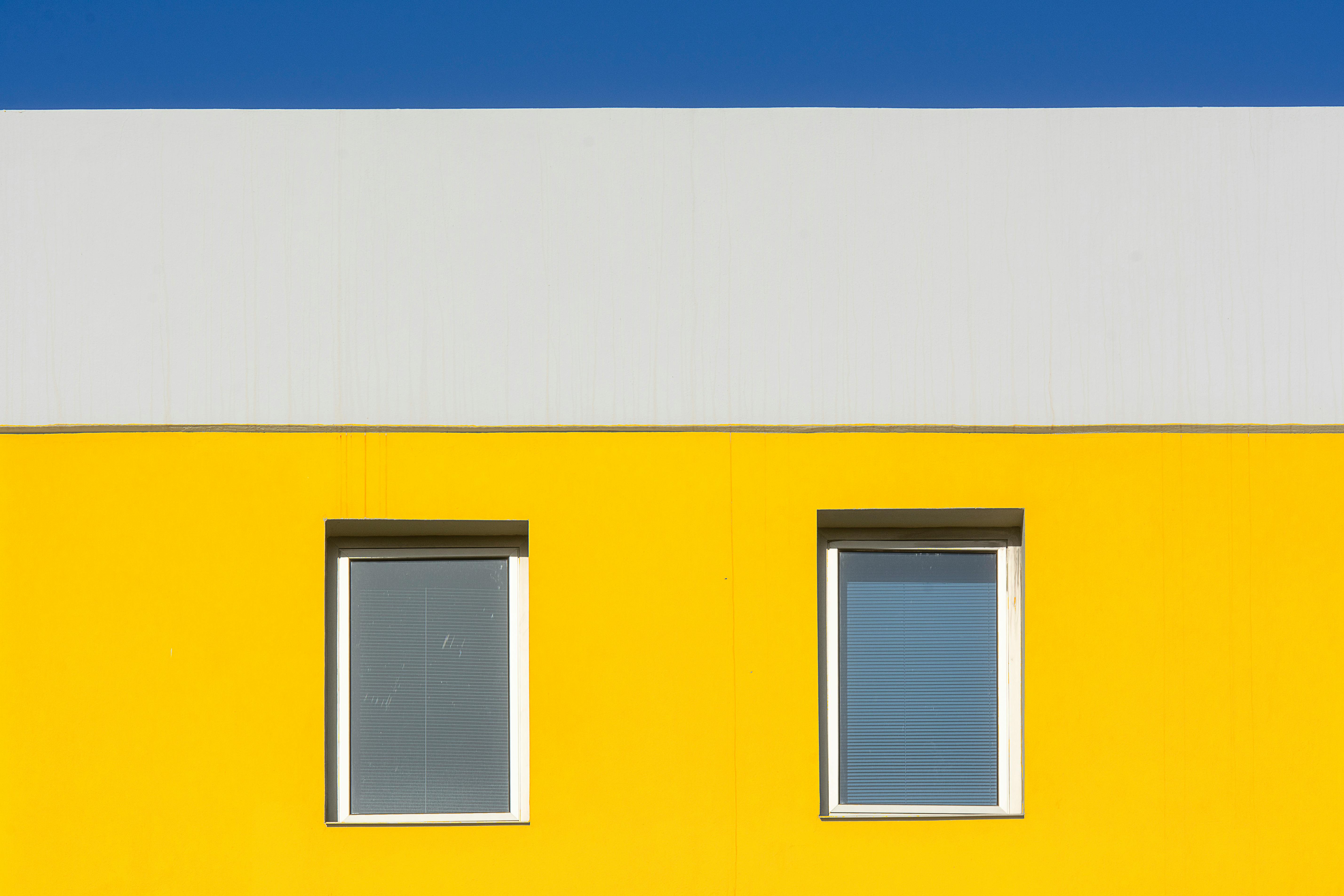 Minimalist architecture featuring a vibrant yellow facade with two windows and a blue sky.
