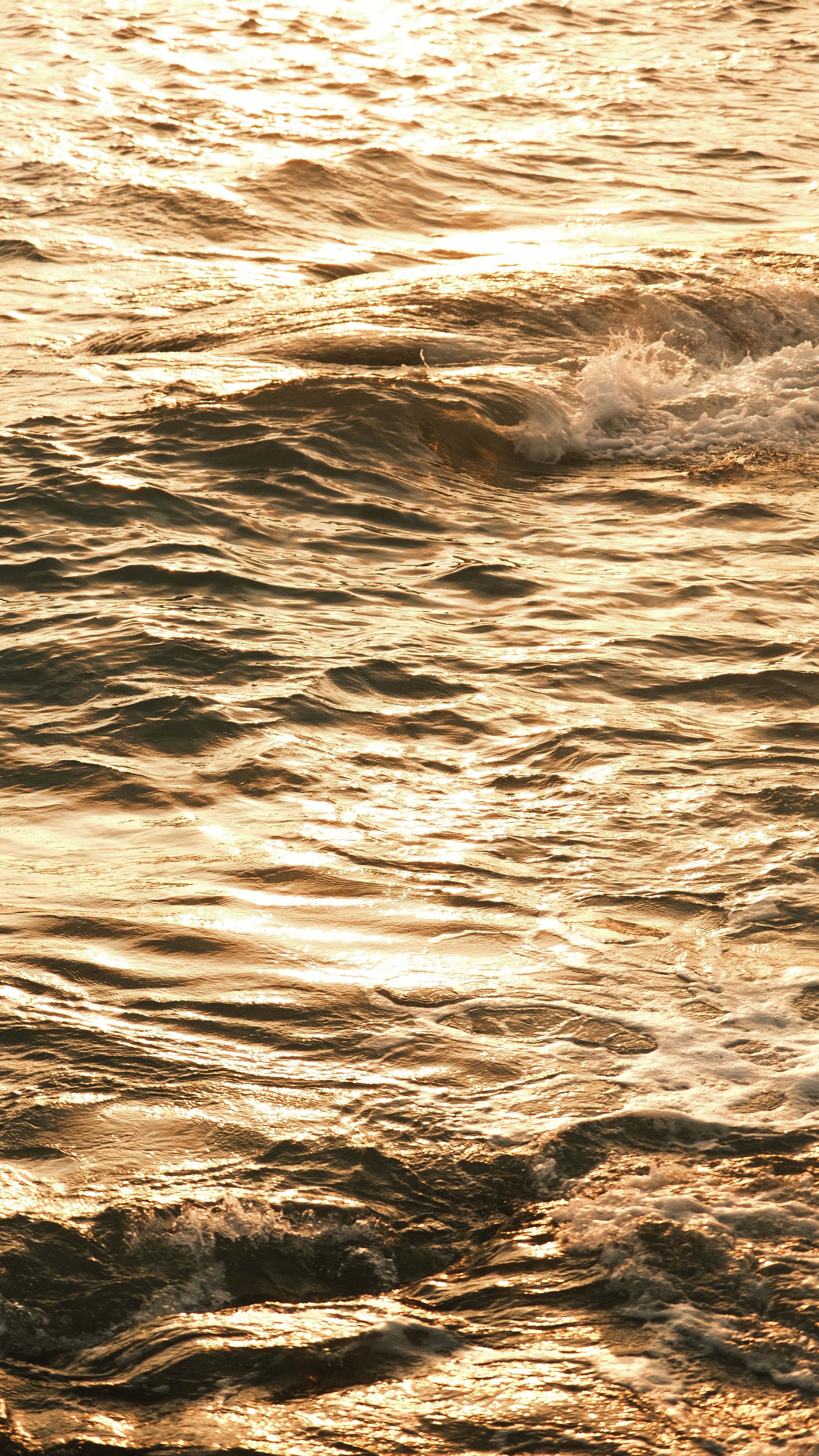 A serene view of sunlit waves creating ripples on the ocean surface at sunset.