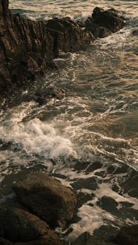 Calm waves gently crashing against rocks on a tranquil shore at sunset.