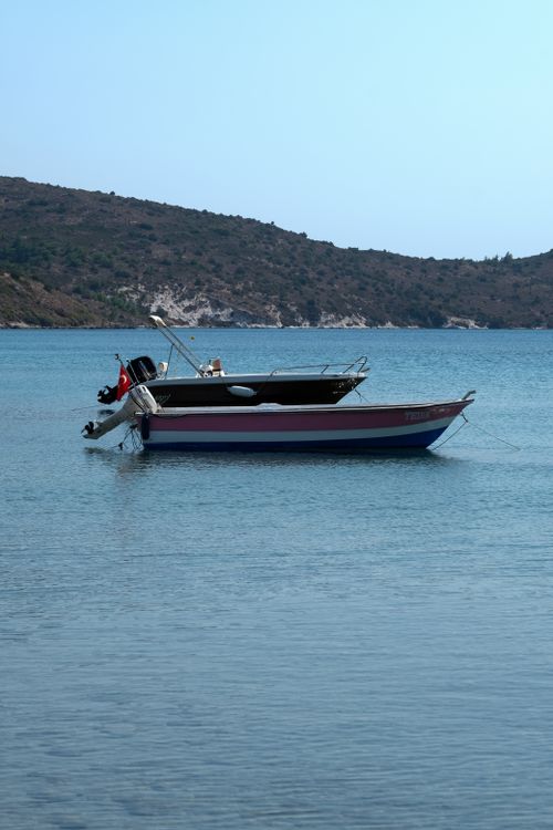 Free A tranquil scene with a small boat anchored in calm blue waters, surrounded by distant hills. Stock Photo
