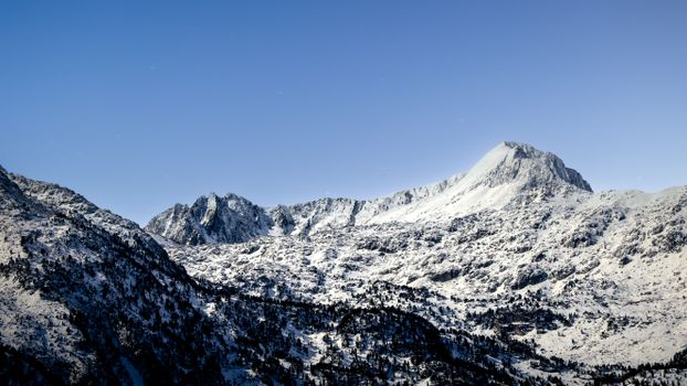 Snow-covered Pyrenees peaks under a starry night sky, showcasing nature's serene beauty.