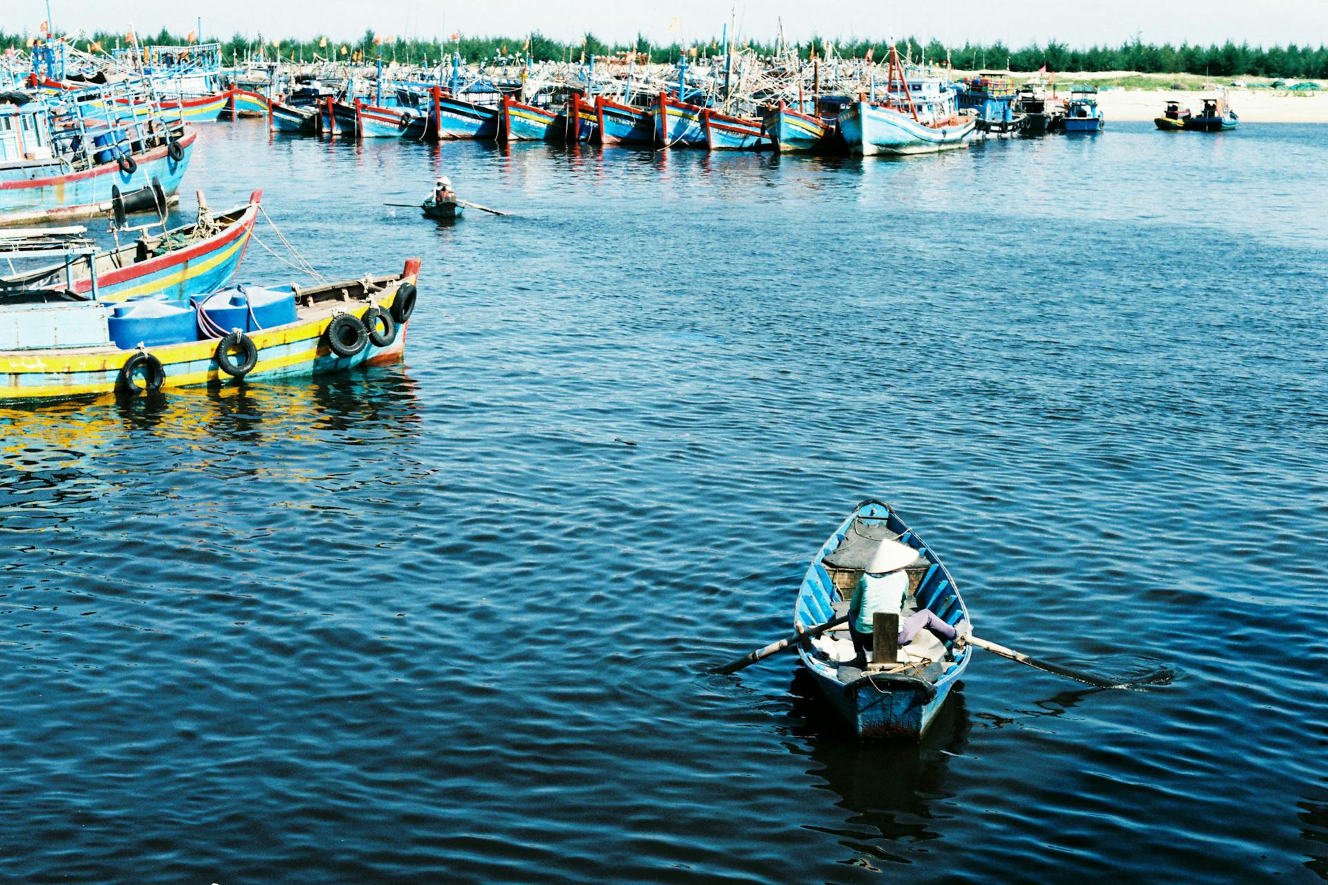 A scenic view of colorful fishing boats docked at Ba Ria Harbor, Vietnam, with a fisherman rowing a small boat.