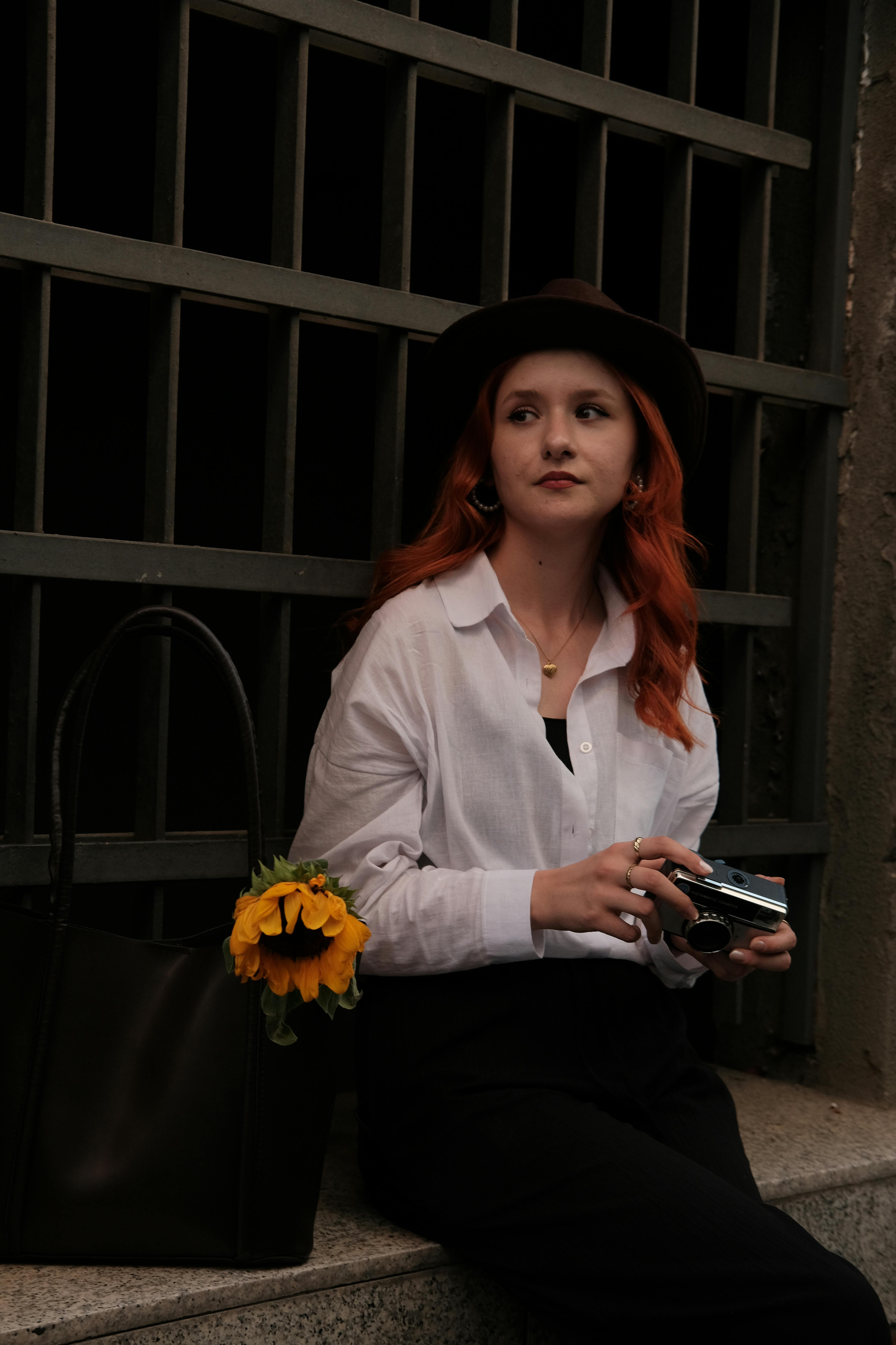 a woman with red hair and a hat is sitting on a ledge