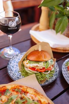 Delicious chicken burger with fresh vegetables and pizza served with red wine.
