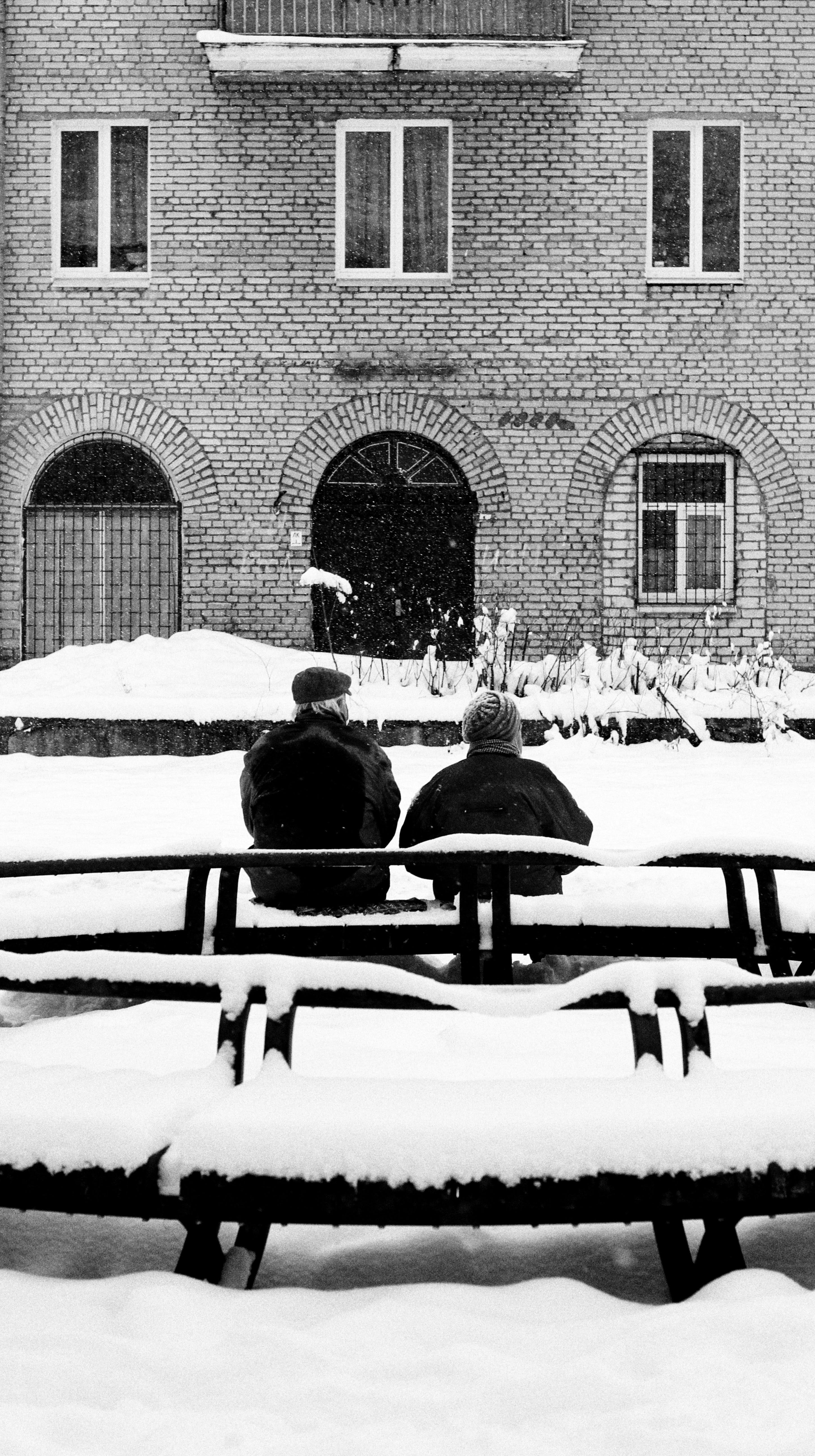 Two adults seated on a snowy street in Minsk, Belarus, during winter.