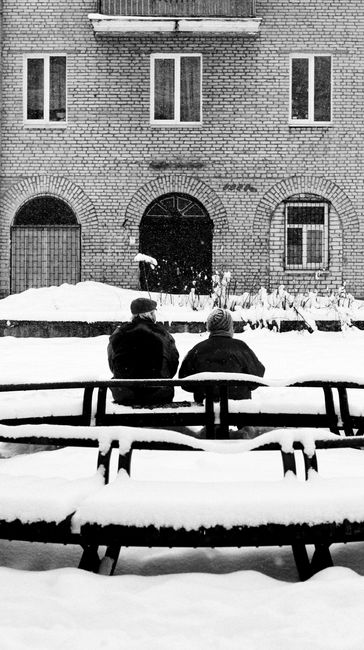 Two adults seated on a snowy street in Minsk, Belarus, during winter.