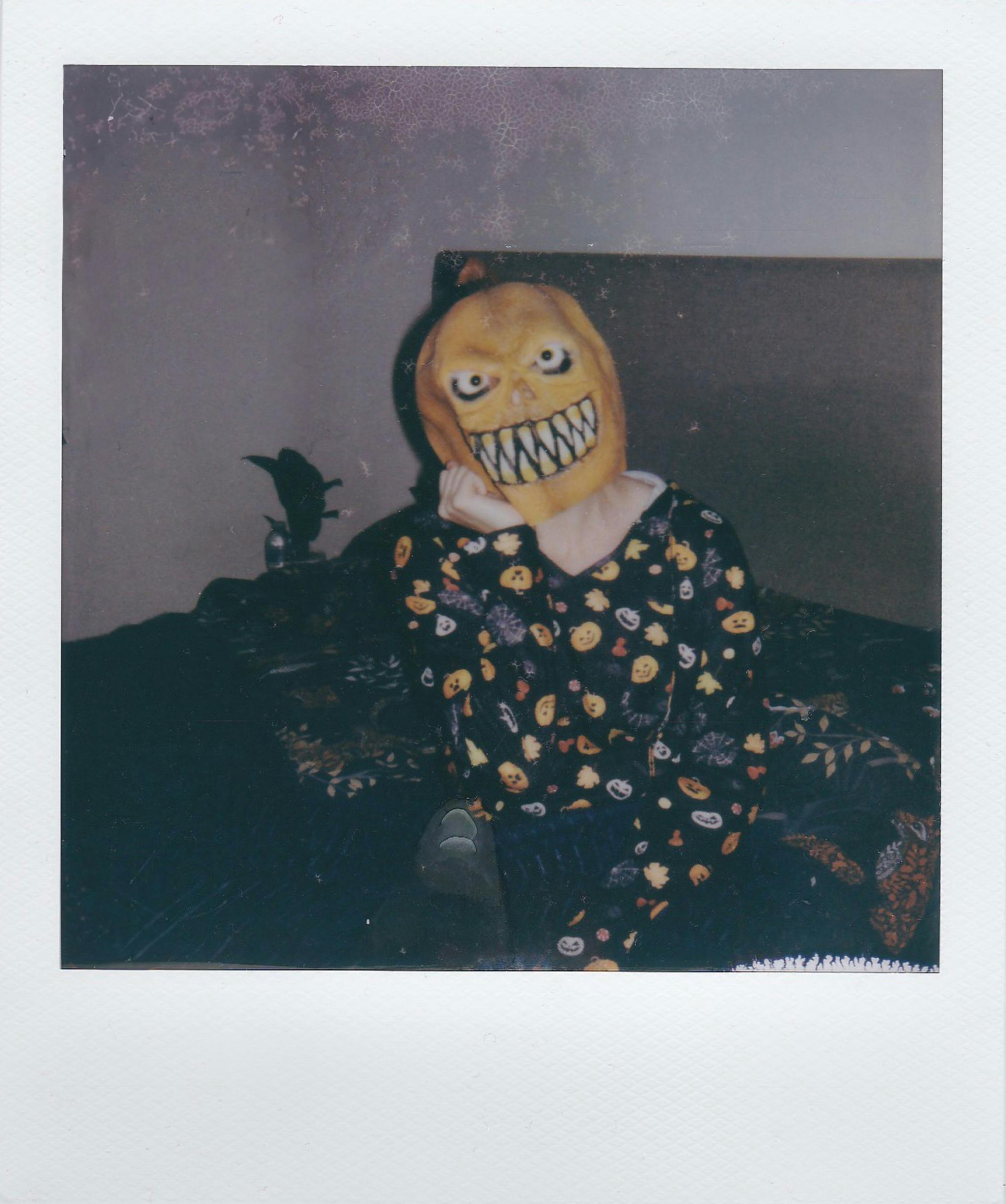 Person wearing a spooky pumpkin mask and Halloween-themed pajamas indoors.