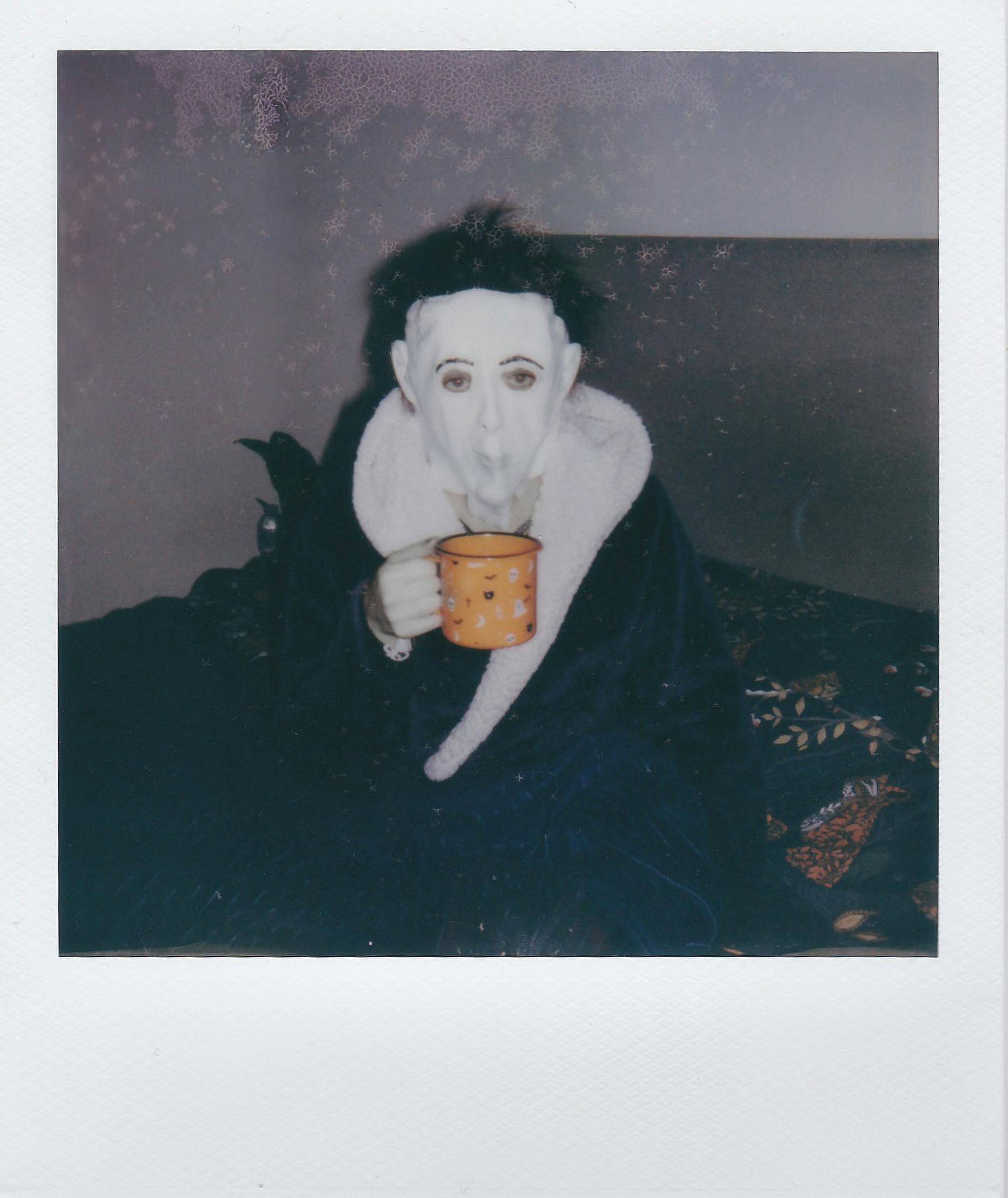 Person in a spooky mask holding a mug indoors. Captures a Halloween ambience.