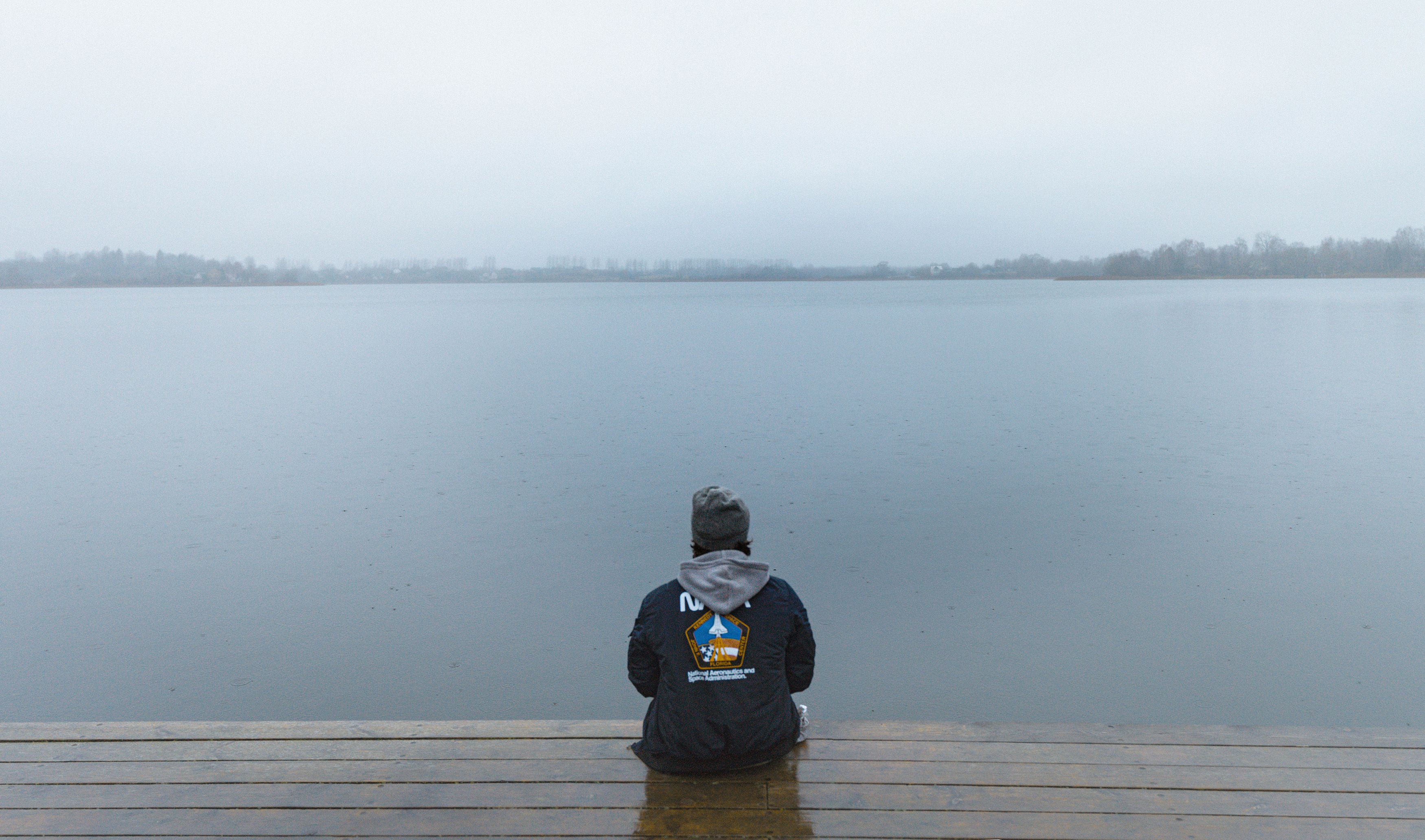 A person sits alone on a dock, reflecting by a misty lake in Belarus.