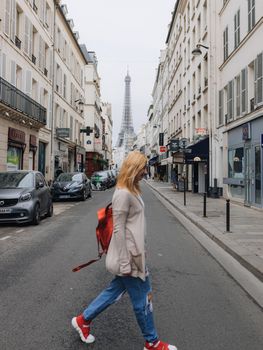 A woman casually crossing a Paris street with the iconic Eiffel Tower in the backdrop, capturing casual urban life.