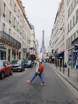 Blond woman walking along a Paris street with the iconic Eiffel Tower in the background, showcasing urban life in France.