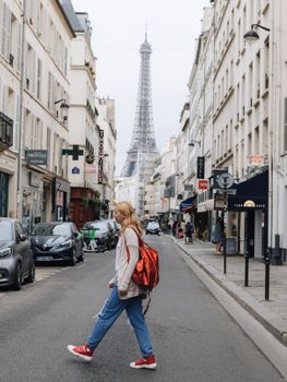Young woman in casual attire walks a Paris street with Eiffel Tower in the background, capturing urban life and architecture.