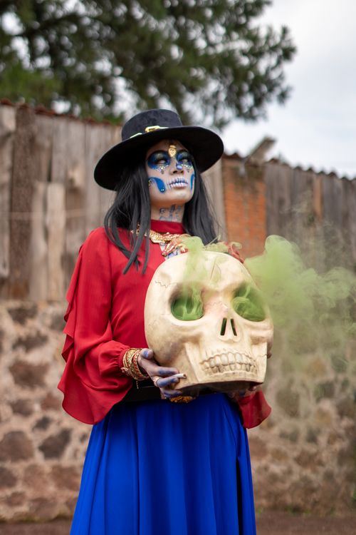 Free Person in Day of the Dead costume holding a large skull emitting green smoke outdoors. Stock Photo