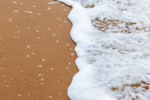 Free Peaceful ocean waves create foam as they wash over a sandy beach, perfect for relaxation themes. Stock Photo