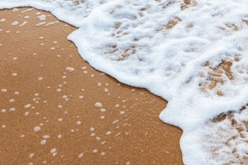 Free Close-up of ocean waves lapping on a sandy beach, creating a soothing summer scene. Stock Photo