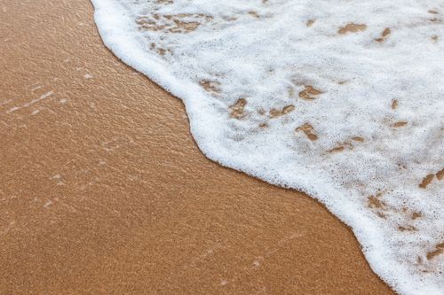 Free Calm waves creating texture on a sandy beach, evoking a serene vacation mood. Stock Photo