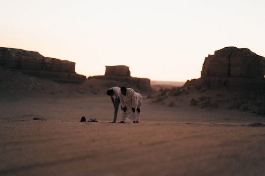 Two people praying in the serene desert landscape of Faiyum Oasis during sunset.