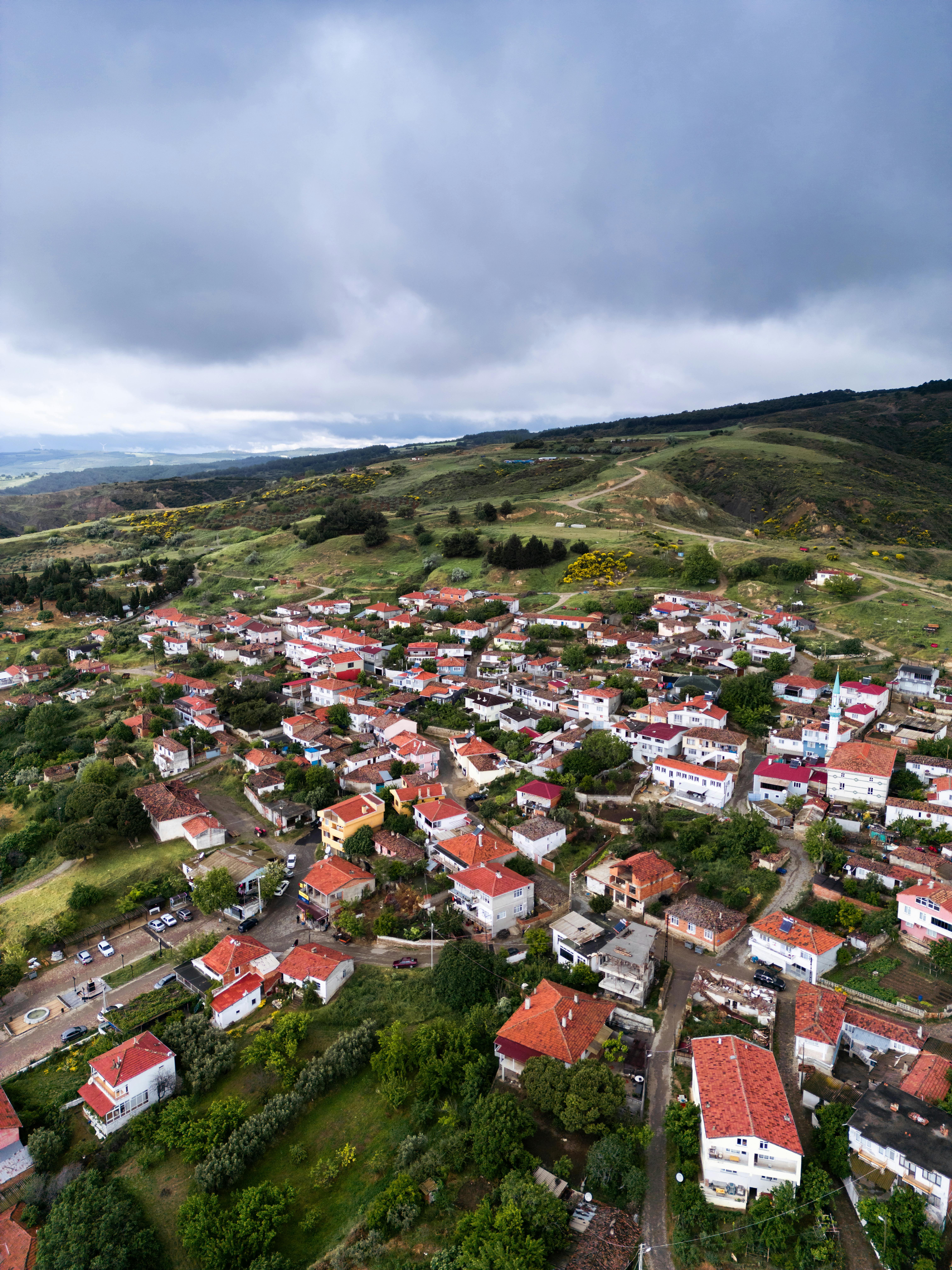 A breathtaking aerial view of a picturesque town with red-tiled roofs surrounded by lush green hills under a cloudy sky.