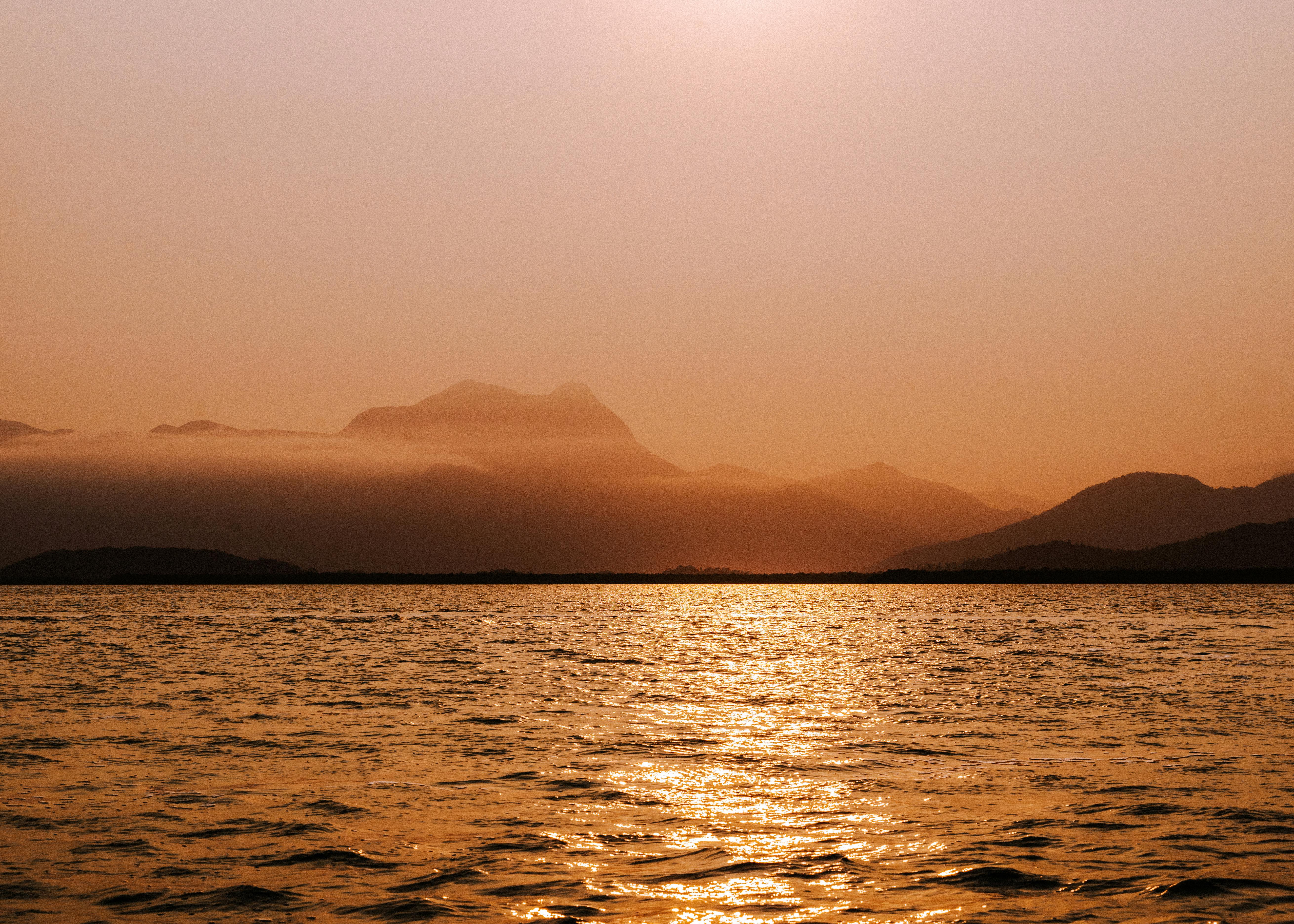 Dramatic sunset over misty mountains and a calm ocean. Perfect for travel and nature themes.