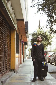 A man strolls along a city street in Lima, Peru, with luggage. Urban travel scene.