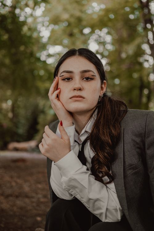 Free Portrait of a stylish woman in a suit, thoughtfully relaxing in a serene park setting during autumn. Stock Photo